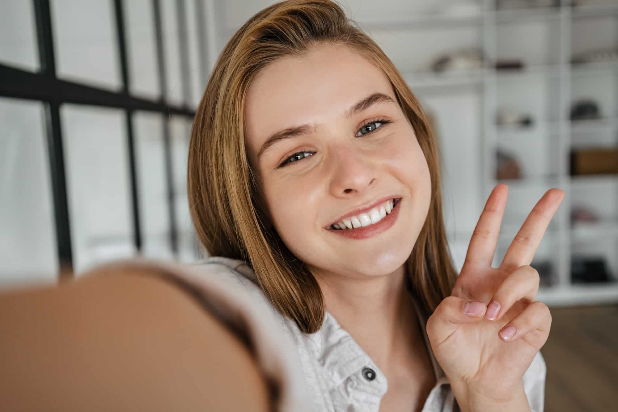 Beautiful joyful nice girl gesturing peace sign while taking selfie